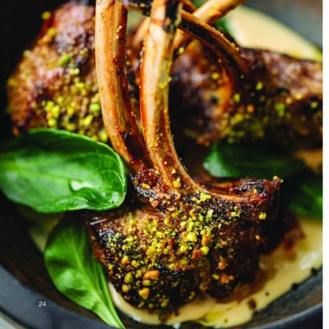 Close-up of herb-crusted lamb chops served with a creamy sauce and garnished with fresh spinach leaves.